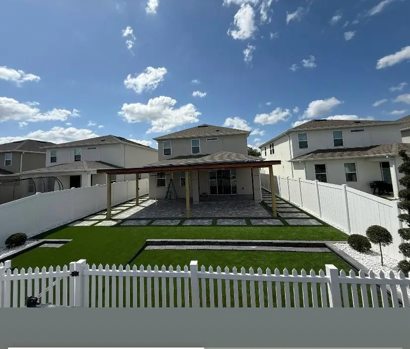 Patio trasero con pérgola de madera, piso de adoquines y grama sintética