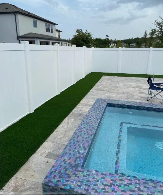 Piscina con spa de mosaico iridiscente, franja de grama sintética y cerco blanco de privacidad